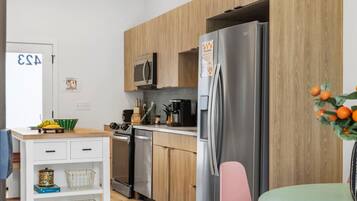 A modern kitchen with wooden cabinets, a stainless steel refrigerator, a microwave, and a dining area with a table and chairs.