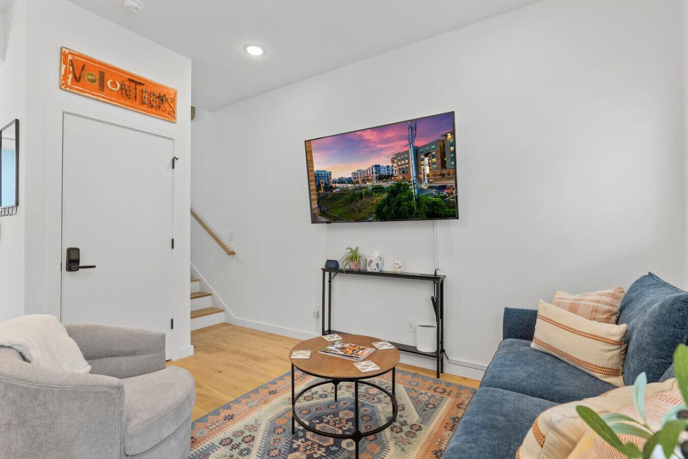 Un salon moderne avec un fauteuil gris, un canapé bleu, une table basse et un tableau représentant un paysage urbain accroché au mur.