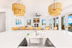 A modern kitchen with a large island, stainless steel sink, and two wicker pendant lights. - Beachfront | Heated Pool | Hot Tub | Fenced Yard with Game Area (Crystal Beach)