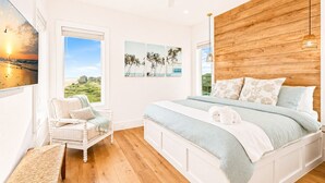 A bedroom with a large bed, a view of the outdoors, a wooden headboard, and a window with a view of palm trees. - Beachfront | Heated Pool | Hot Tub | Fenced Yard with Game Area (Crystal Beach)