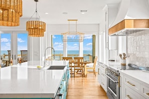 A modern kitchen with a large island, white cabinetry, and a view of the ocean. - Beachfront | Heated Pool | Hot Tub | Fenced Yard with Game Area (Crystal Beach)
