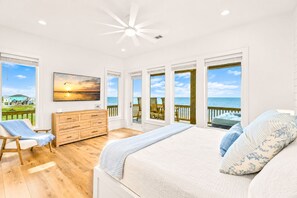 A bedroom with a large bed, a wooden dresser, a chair, and a painting of a sunset. - Beachfront | Heated Pool | Hot Tub | Fenced Yard with Game Area (Crystal Beach)