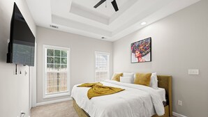 A bedroom with a bed, a TV, two windows with blinds, a ceiling fan, and a painting on the wall. - Breath of Fresh Air DT Atlanta (Atlanta)