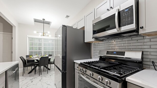 A modern kitchen with stainless steel appliances, a marble floor, and a dining area with black chairs and a white table. - Breath of Fresh Air DT Atlanta (Atlanta)