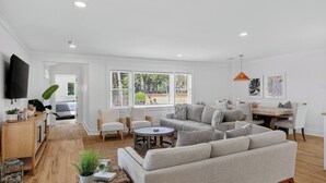 A modern living room with a sofa, chairs, a coffee table, and a dining area with a table and chairs. - 16 29th Avenue Isle of Palms Group Retreat (Isle of Palms)