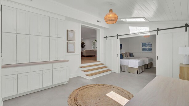 A modern interior with white cabinetry, a staircase, a dining area, and a bedroom with a bed and a nightstand. - 16 29th Avenue Isle of Palms Group Retreat (Isle of Palms)