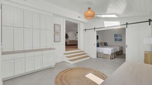 A modern interior with white cabinetry, a staircase, a dining area, and a bedroom with a bed and a nightstand. - 16 29th Avenue Isle of Palms Group Retreat (Isle of Palms)