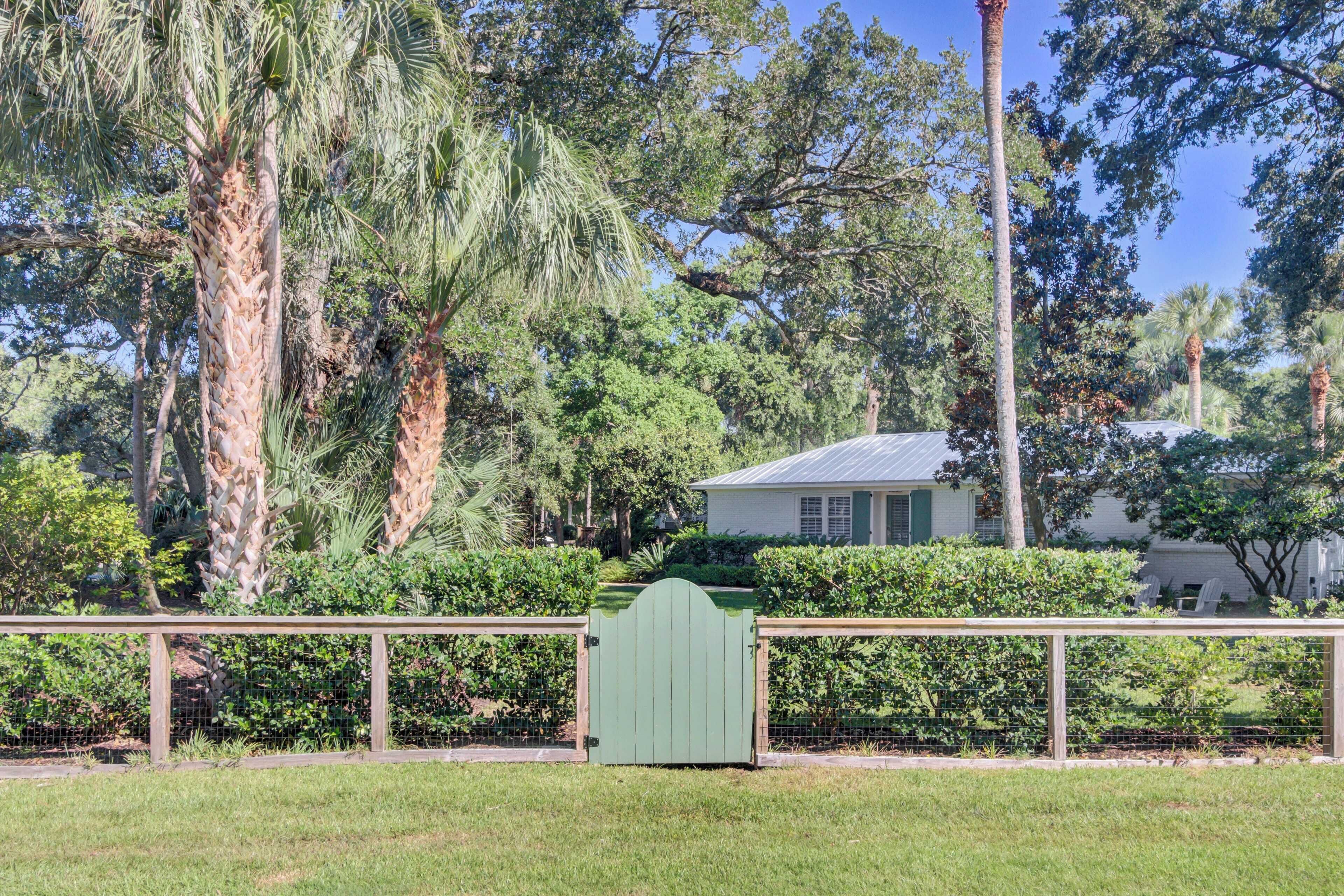 Un espace clos, délimité par un portail vert, et entouré d’une végétation luxuriante et de grands arbres.