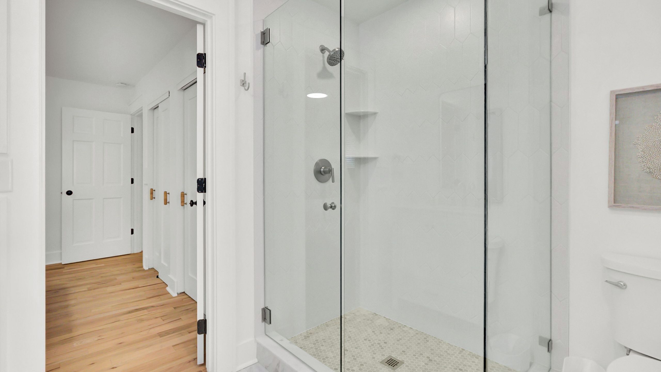 A modern bathroom with a glass shower enclosure, a white toilet, and a wooden floor.