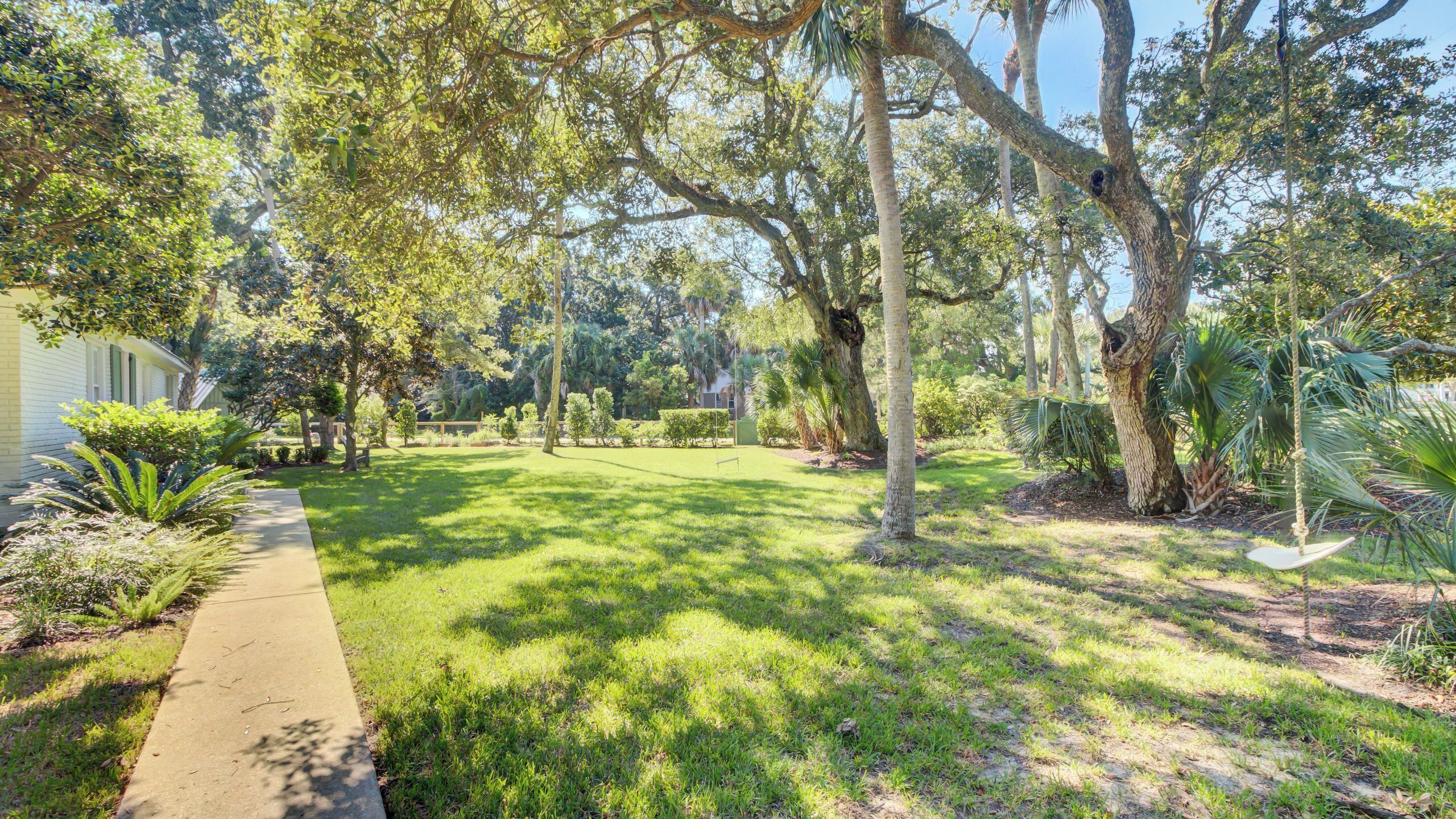 A well-maintained garden with a pathway leading to a house, surrounded by mature trees and various plants.