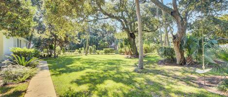 A well-maintained garden with a pathway leading to a house, surrounded by mature trees and various plants.