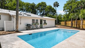 A swimming pool with a patio area, a grill, and outdoor seating.