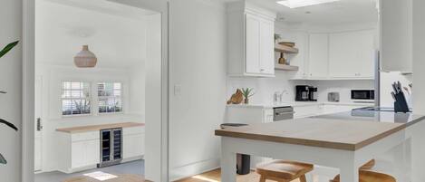 Una cocina moderna con armarios blancos, una isla central con taburetes y un tragaluz.