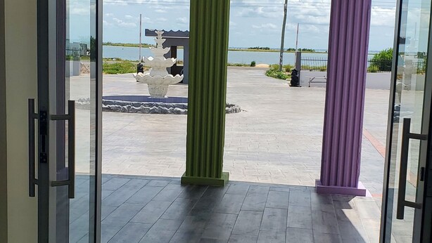 A glass door entrance with a view of a paved outdoor area, including a water feature and a distant body of water.