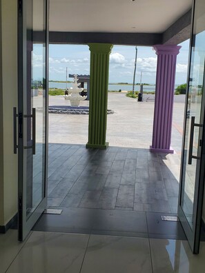 A glass door entrance with a view of a paved outdoor area, including a water feature and a distant body of water. - LAGOON BEACH HOTEL  (Keta)