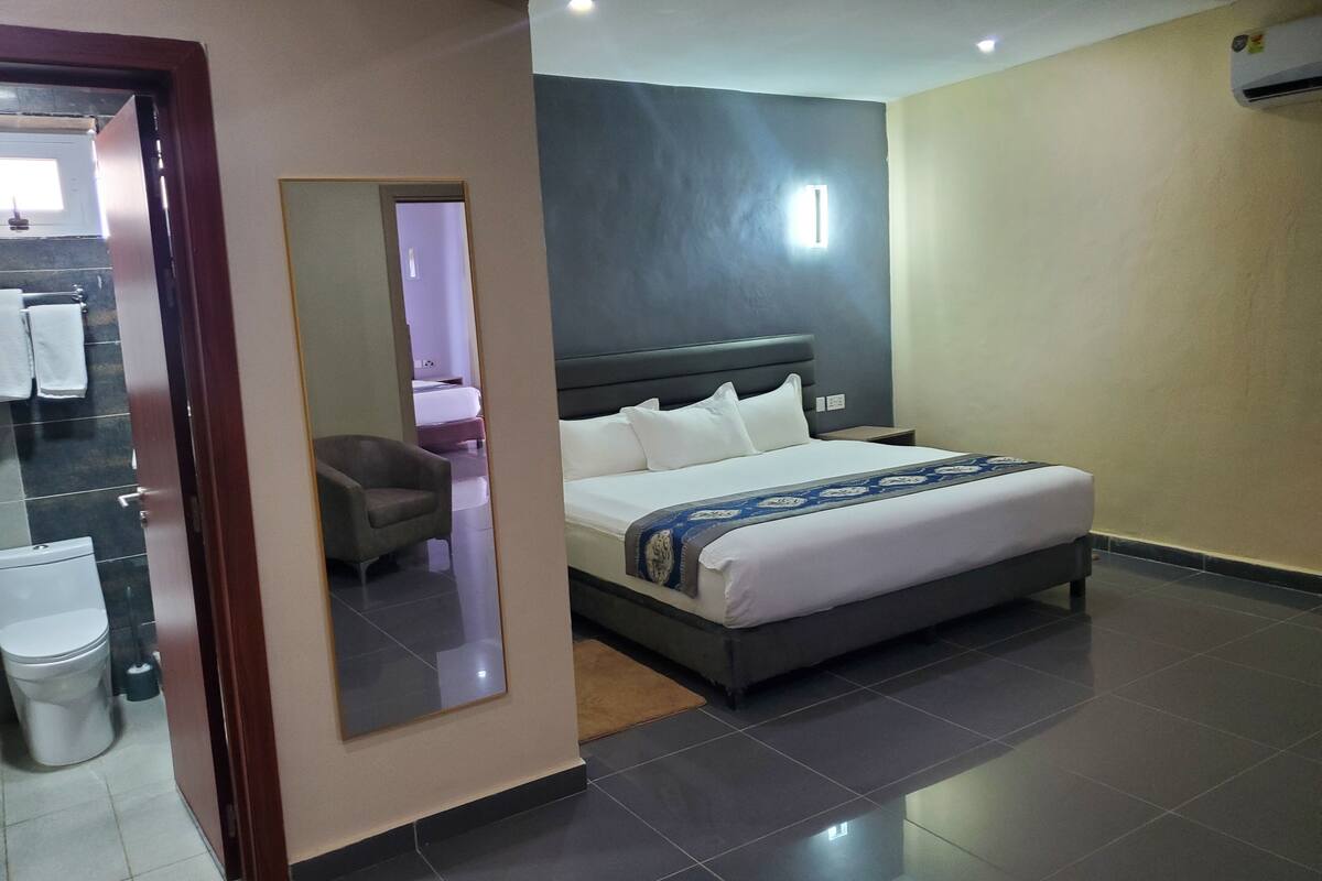 A hotel room with a large bed, a bedside table, a mirror, and a view of the bathroom.