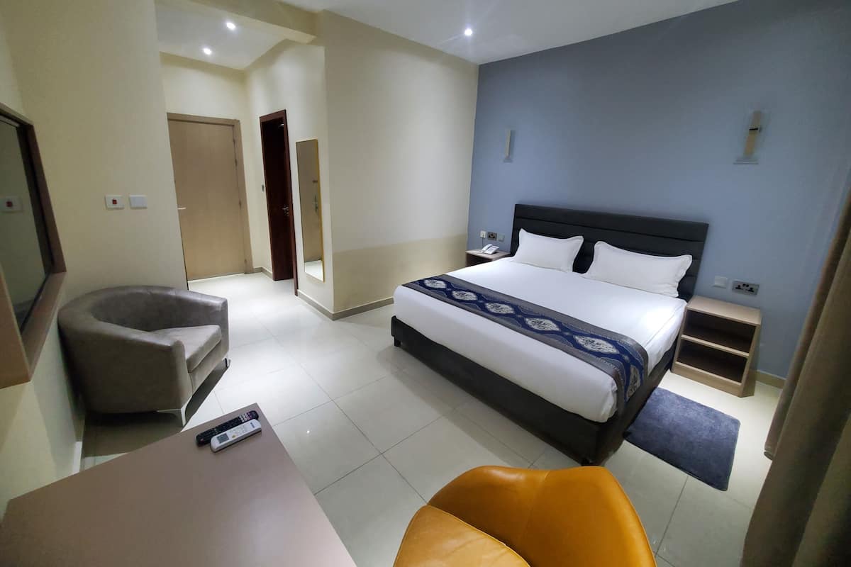 A hotel room with a bed, bedside table, chair, and a desk with a remote control.