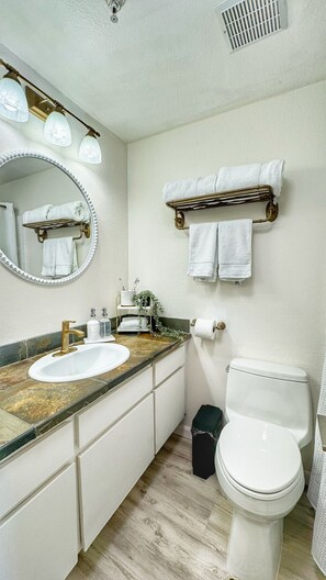 A bathroom with a sink, mirror, towel rack, toilet, and trash bin. - NEW Steps from Sand with Breathtaking Views @PB (San Diego)