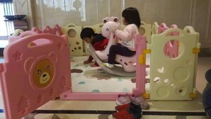 Un espace de jeux pour enfants avec une structure de jeu rose et blanche, comprenant une porte en forme d’ours et une aire de jeux circulaire.