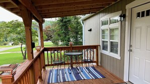 A wooden deck with a small table and two chairs, a white door, and a view of a green landscape.