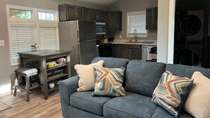 A compact living space with a gray sofa, a small dining table, and a kitchen area with dark cabinets and appliances.