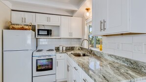 A modern kitchen with white cabinetry, a granite countertop, a built-in oven, a microwave, and a sink.