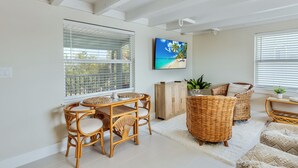 A bright living room with a dining table, wicker furniture, and a TV on the wall.