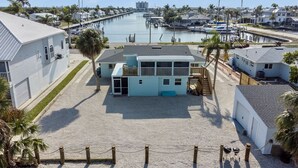 A beachfront property with a large house, a dock, and a marina in the background.