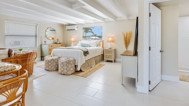 A bedroom with a bed, bedside tables, a mirror, a window with blinds, a door, and a view of the outside.