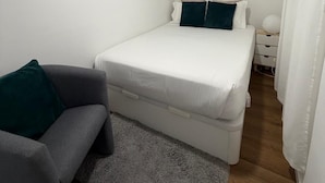 A small, clean room with a bed, a gray sofa, a small table, and a white curtain. - Nove de Julho Apartment (Porto)