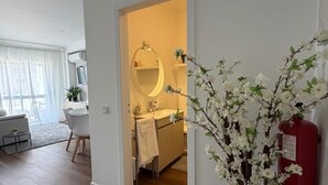 A modern living room with a sofa, a dining table, and chairs. There is a hallway leading to a bathroom with a mirror and sink. - Nove de Julho Apartment (Porto)