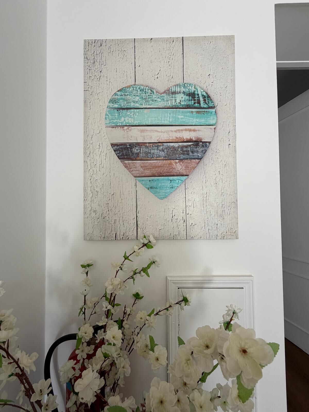 A wall-mounted heart-shaped artwork with a distressed wood texture and a color palette of white, teal, and brown.