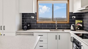 Een moderne keuken met uitzicht door het raam, zwart-wit betegelde vloer en een koffiezetapparaat.