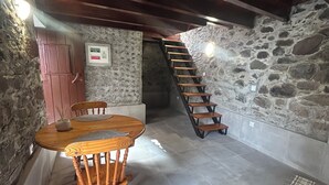 Um quarto rústico com uma mesa e cadeiras de madeira, uma parede de pedra, uma escada de madeira e um pequeno tapete no chão.