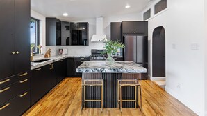 Una cocina moderna con armarios oscuros, encimera de mármol y una isla central con taburetes.