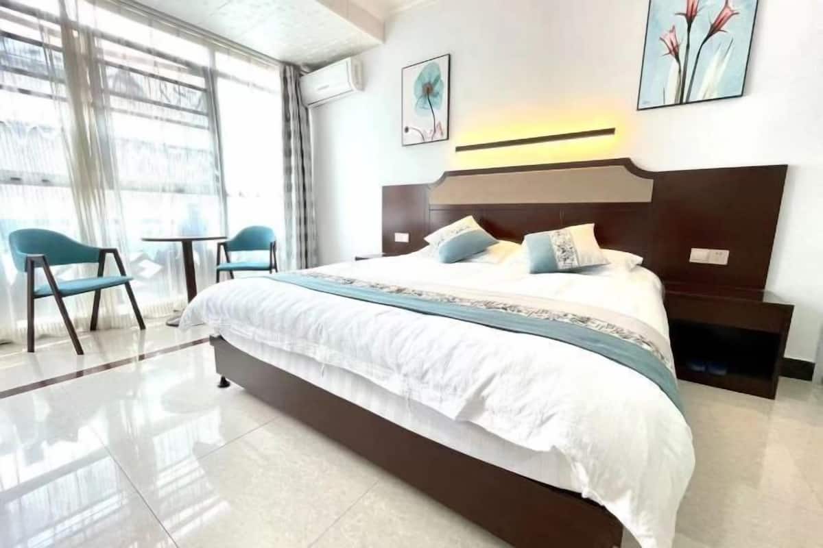 Una habitación de hotel moderna con una cama grande, dos sillones, una mesita pequeña y obras de arte en las paredes.