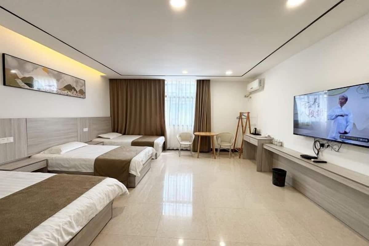 Habitación de hotel con tres camas, televisión, escritorio y una silla.
