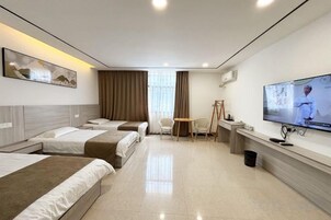 Una habitación de hotel con cuatro camas, un escritorio, un televisor y una ventana con cortinas.