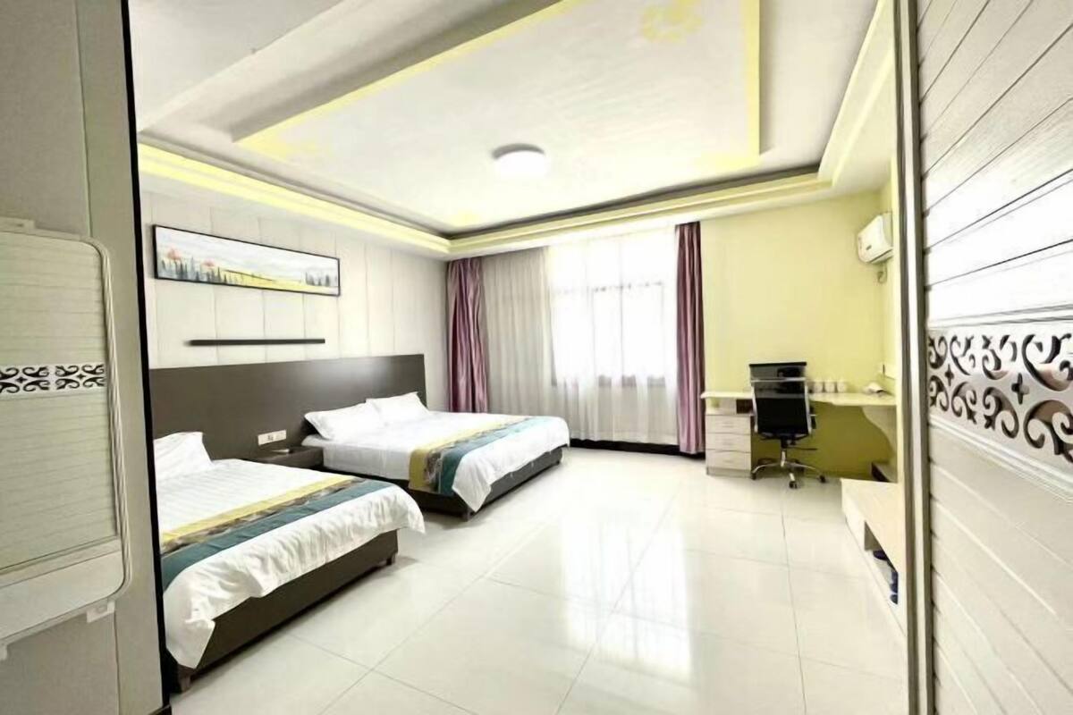 Habitación de hotel con dos camas, un escritorio, una silla, una ventana con cortinas e iluminación en el techo.