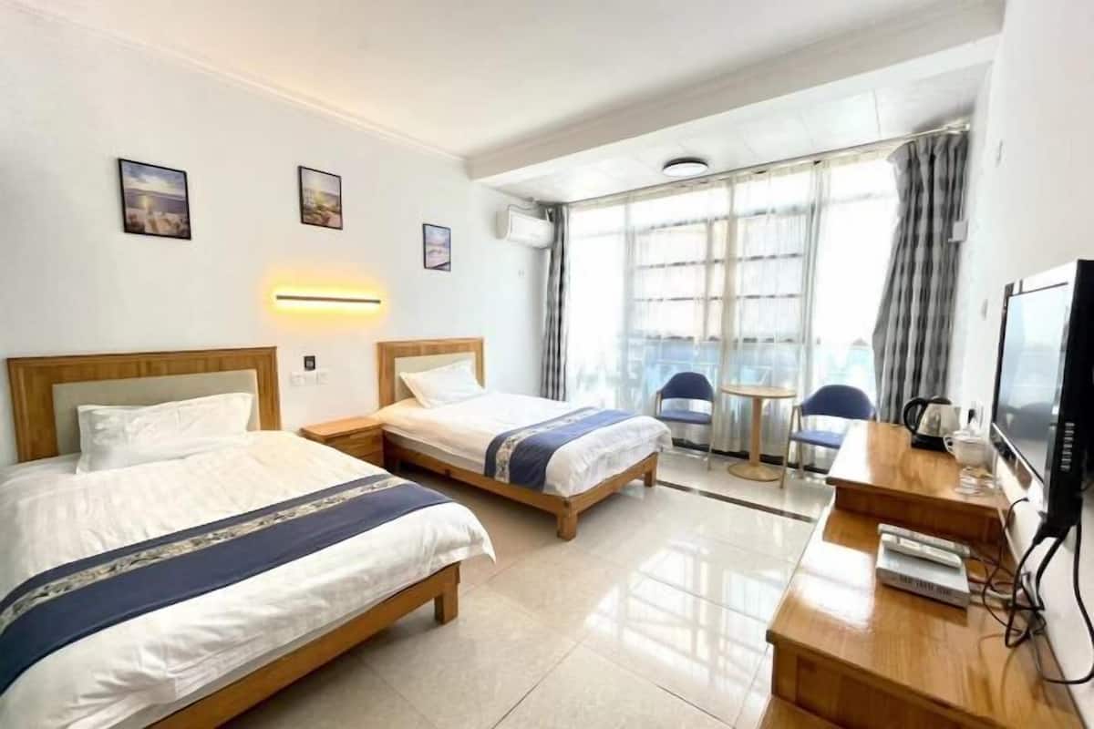 Habitación de hotel con dos camas, un escritorio, una silla, un televisor y una ventana con cortinas.
