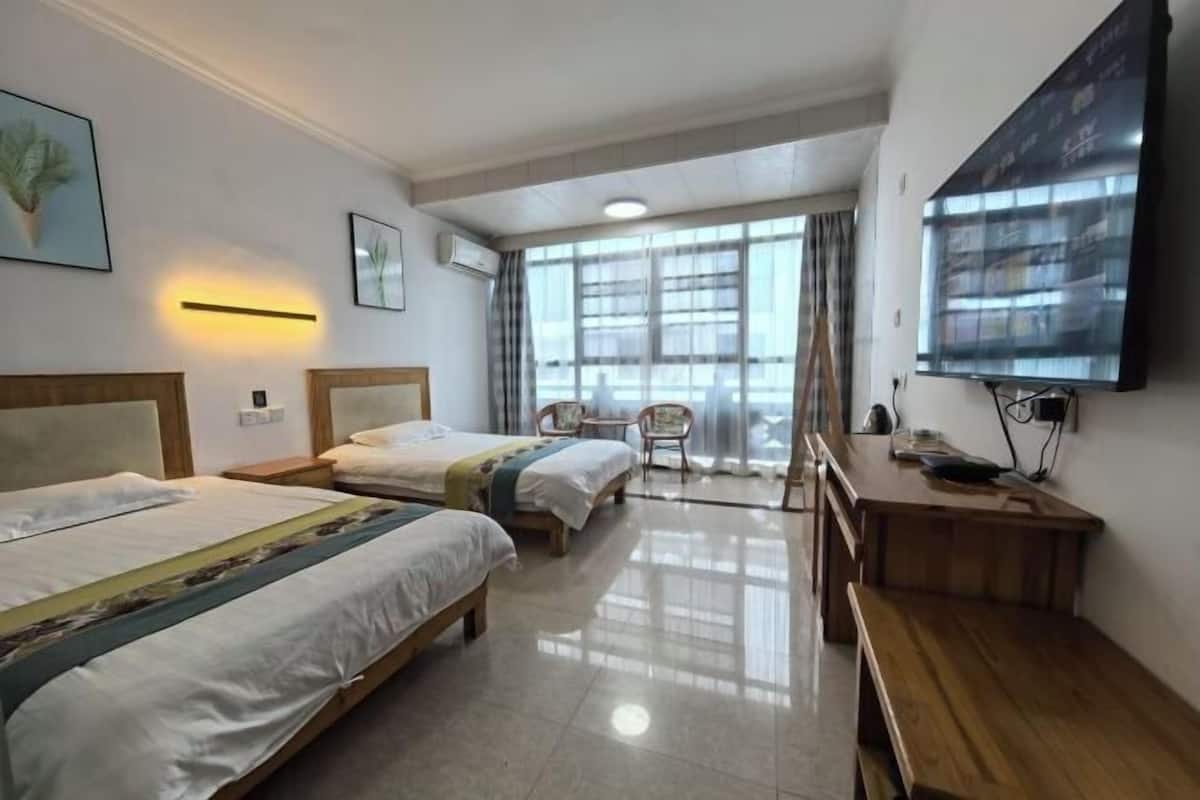 Habitación de hotel con dos camas, un escritorio, una silla, un televisor y un ventanal grande.
