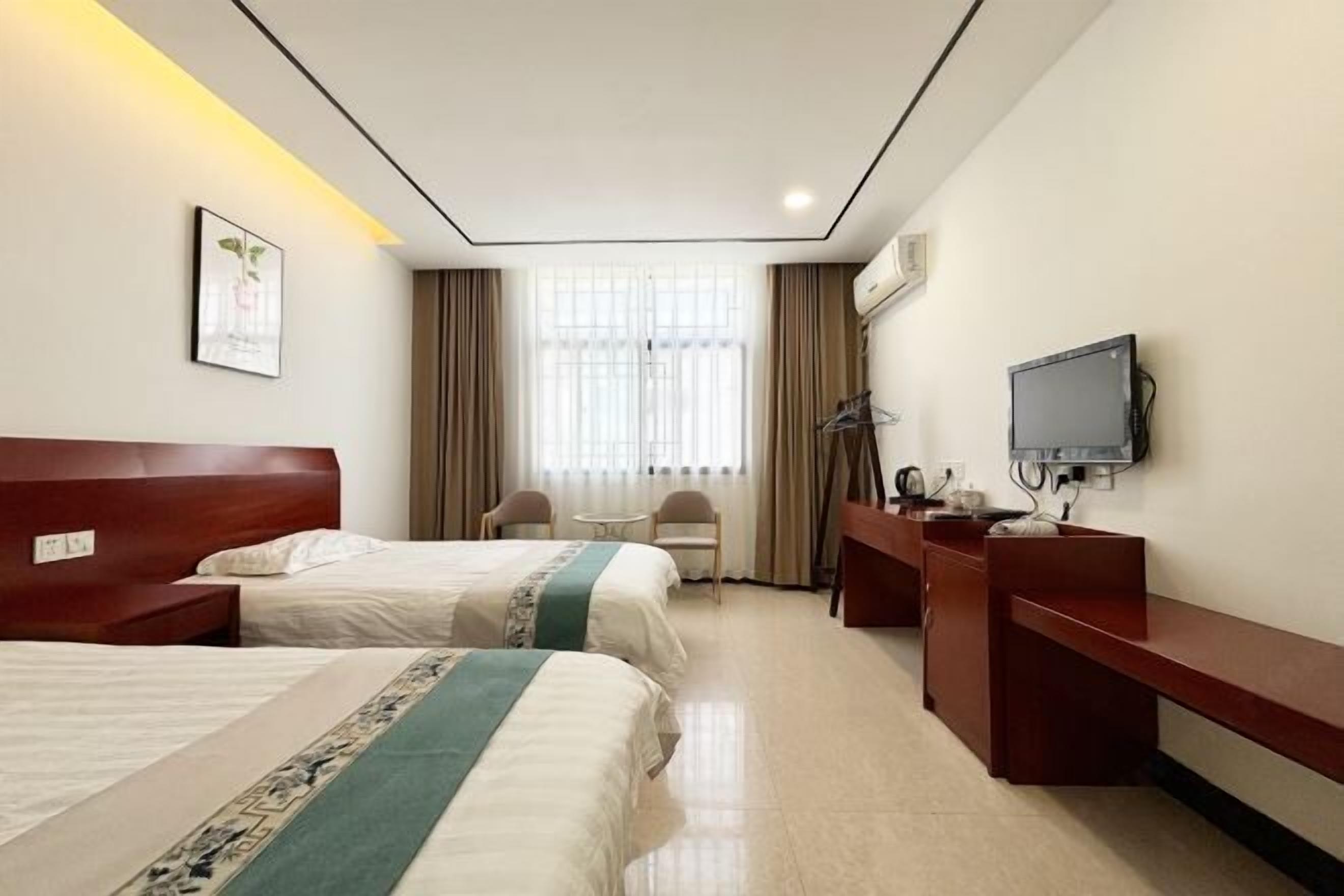 Habitación de hotel con dos camas, un escritorio, una silla, un televisor y una ventana con cortinas.