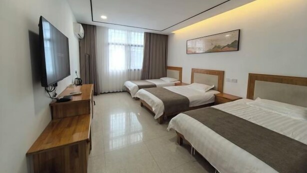 Una habitación de hotel con tres camas, televisión, escritorio y un cuadro en la pared.