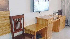 Un escritorio de madera con una silla, un televisor montado en la pared y un mueble pequeño con zapatos.
