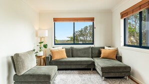 A modern living room with a sectional sofa, a floor lamp, and a view of trees through large windows.