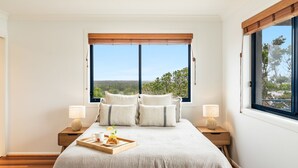 A bedroom with a large bed, two bedside tables with lamps, a tray with breakfast items, and a view of greenery through a window.