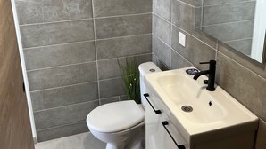 Ein Badezimmer mit grauen Fliesen, einer weißen Toilette, einem beigen Waschbecken mit schwarzem Wasserhahn und einem Spiegel über dem Waschbecken.