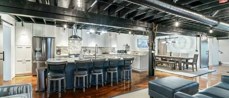 A modern kitchen with a central island, bar stools, and a dining area with a table and chairs.