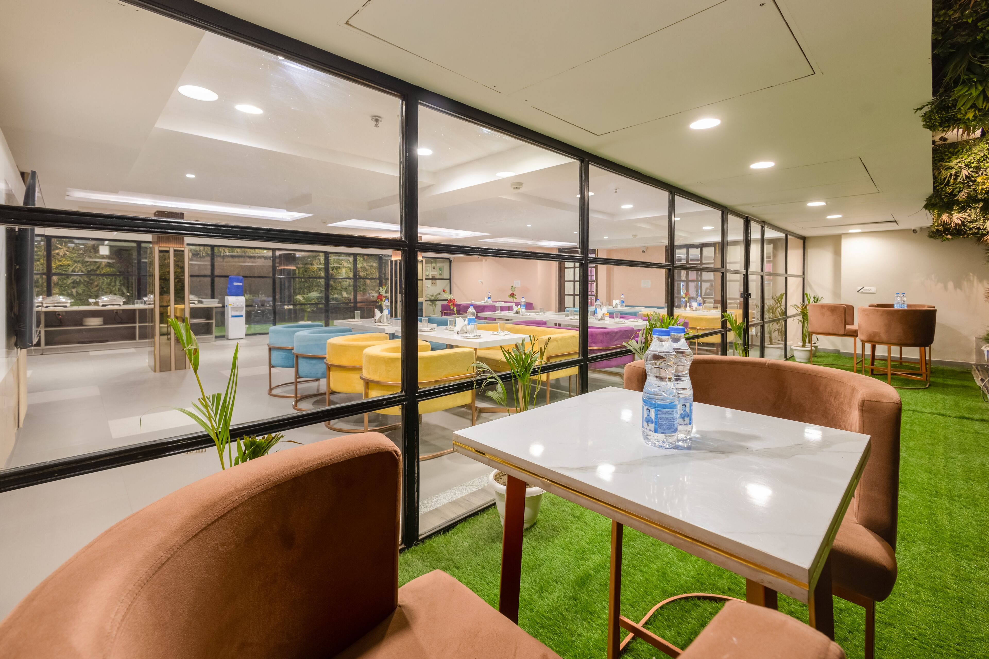 A modern indoor space with glass walls, green artificial turf, and various seating arrangements.