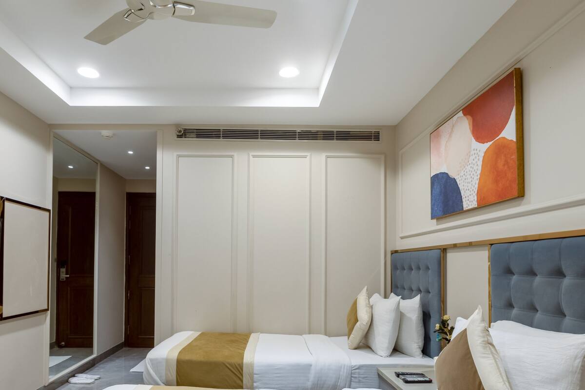 Hotelkamer met plafondventilator, twee bedden, nachtkastje, schilderij en een deur naar een andere kamer.